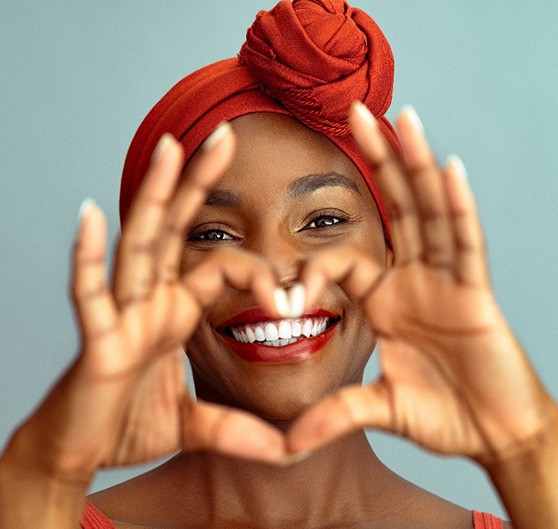 Woman using her fingers to make a heart shape around her smile