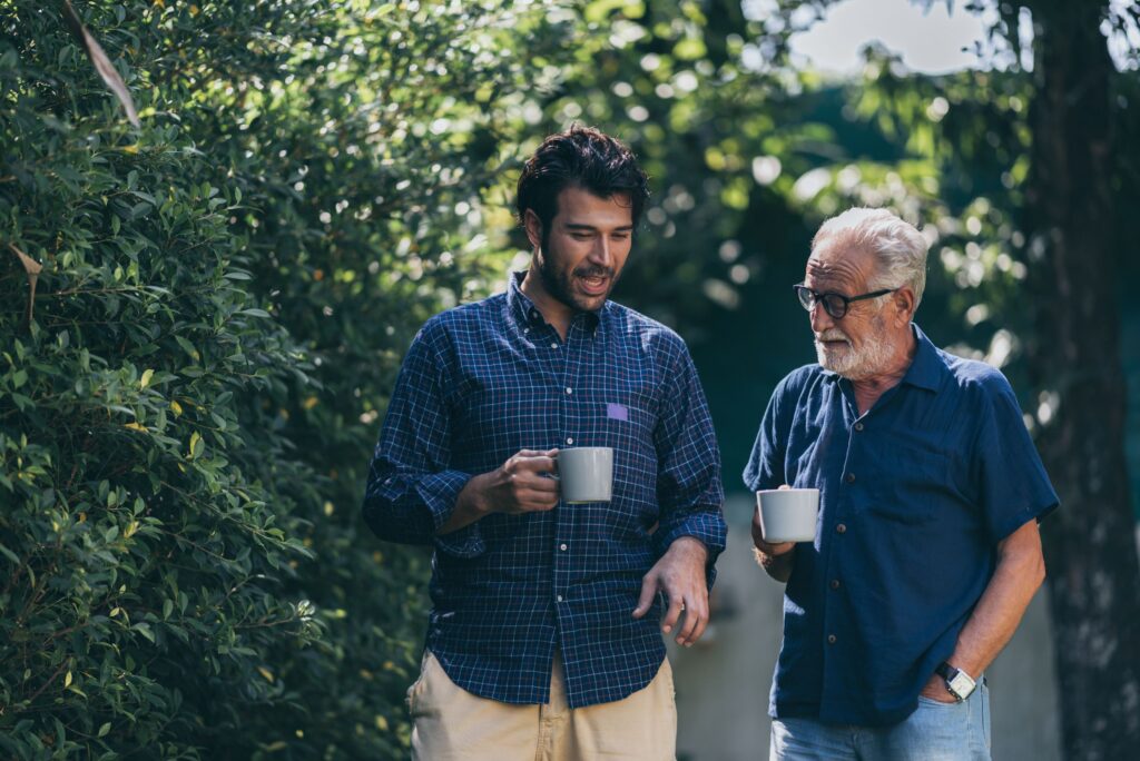 Younger man and older man in blue shirts outside chatting over coffee